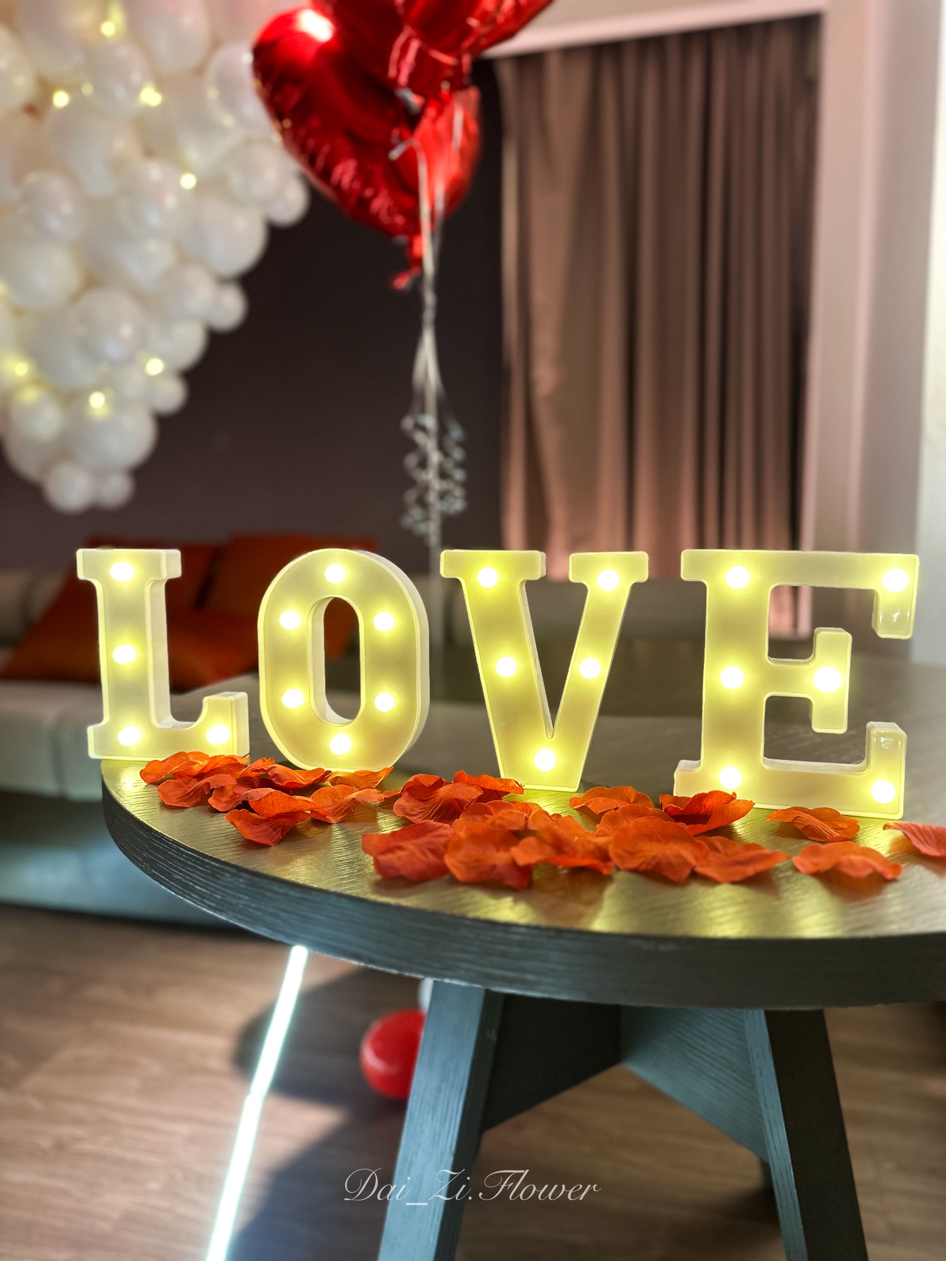 求婚佈置細節，桌面擺放發光LOVE字母與散落的浪漫紅花瓣。