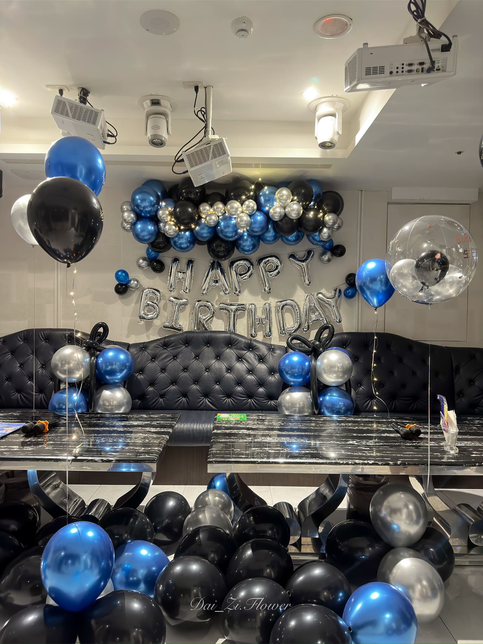 DAIZI 代紫花藝全景生日會場佈置，地面鋪滿藍黑銀三色氣球，沙發區設置氣球立柱增添層次感。