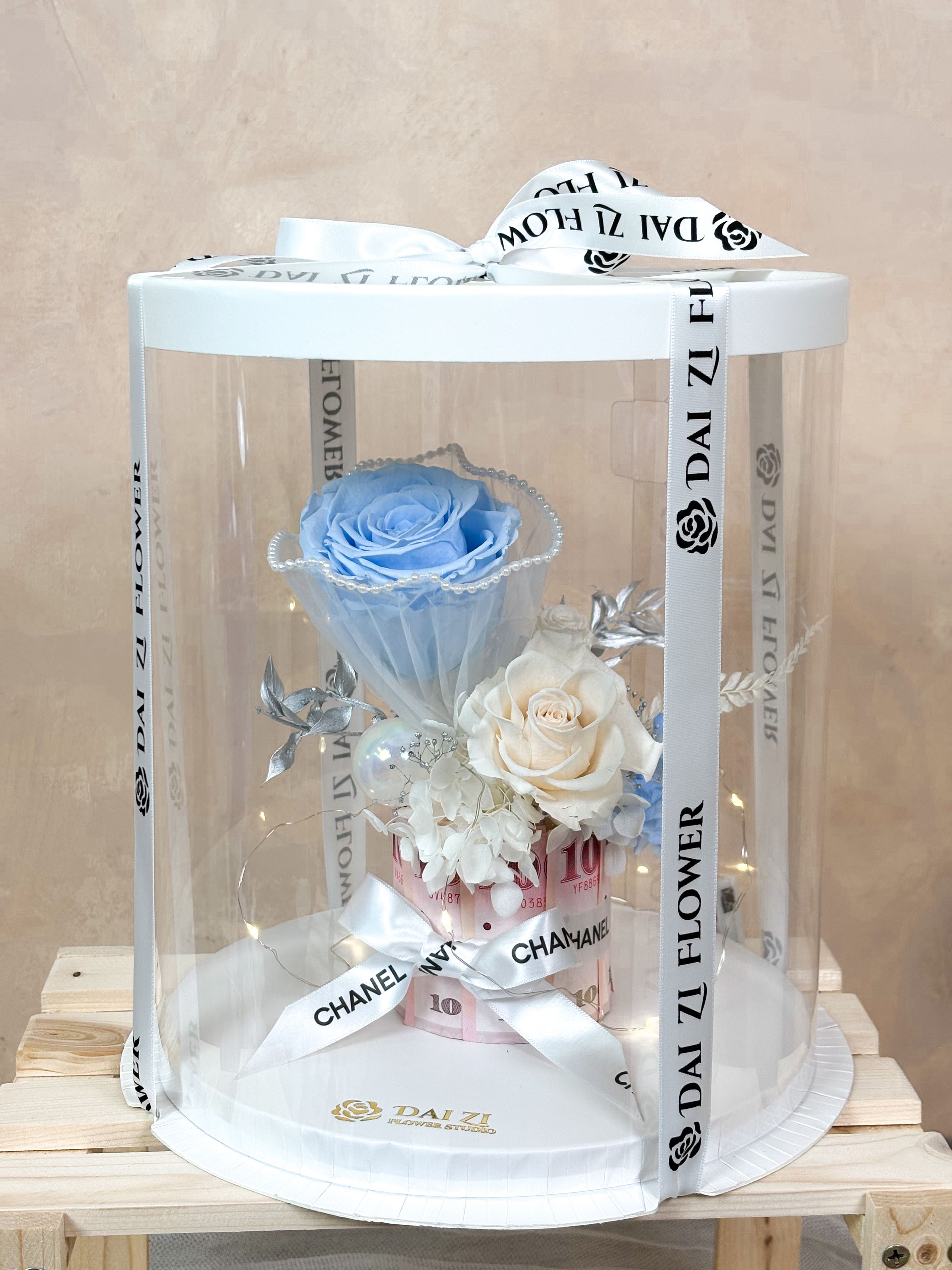 精品級永生花鈔票蛋糕透明圓型禮盒，大台北 DAIZI代紫花藝專屬訂製，讓清新藍色系有錢花在精品包裝下更顯質感，成為永恆珍藏的專屬浪漫禮物。
