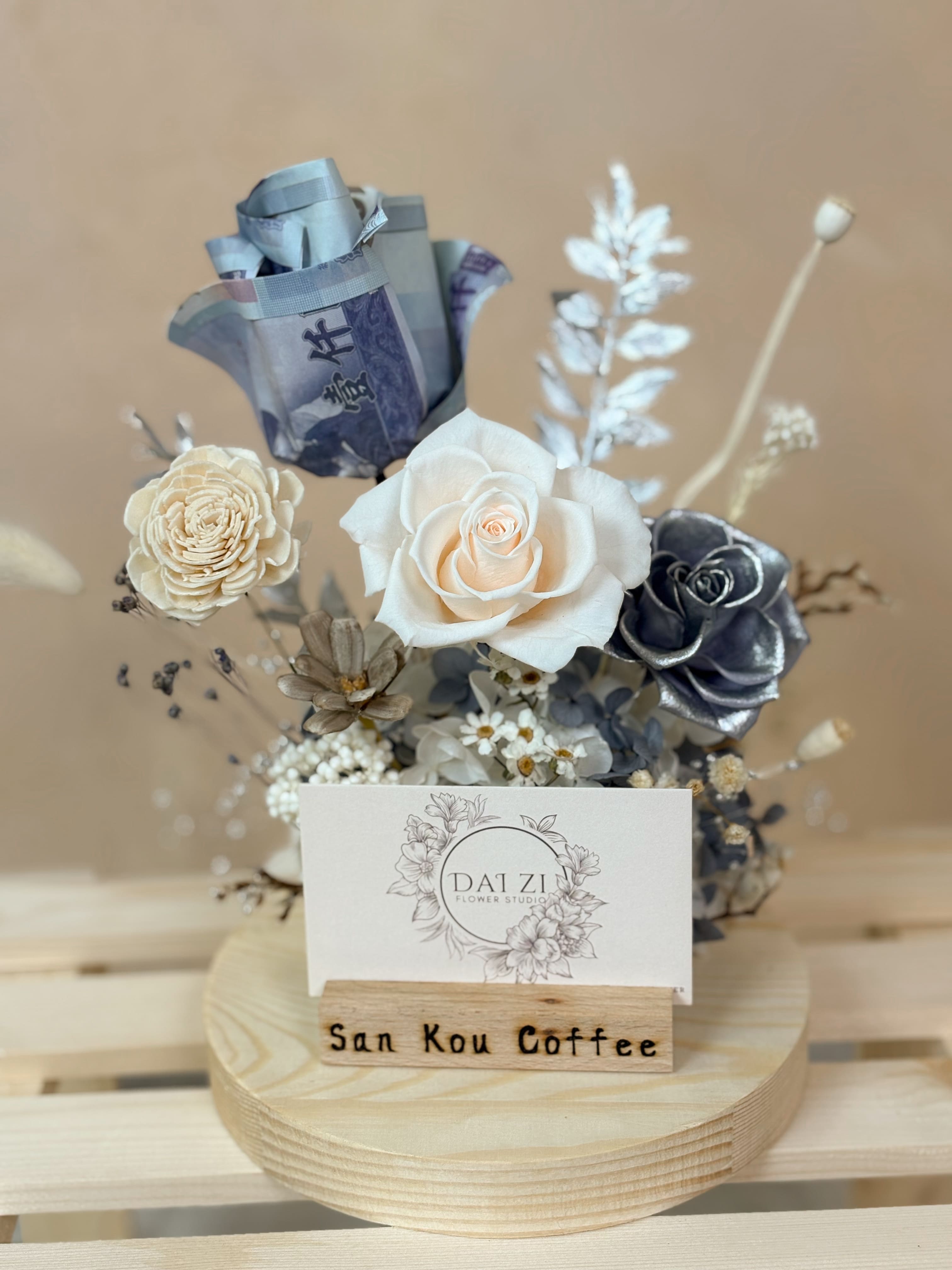 DAIZI 代紫花藝為 San Kou Coffee 訂製之銀河系永生花名片座，結合特殊銀白色系玫瑰與千元鈔票摺製的有錢花，展現極致奢華的開幕送禮質感