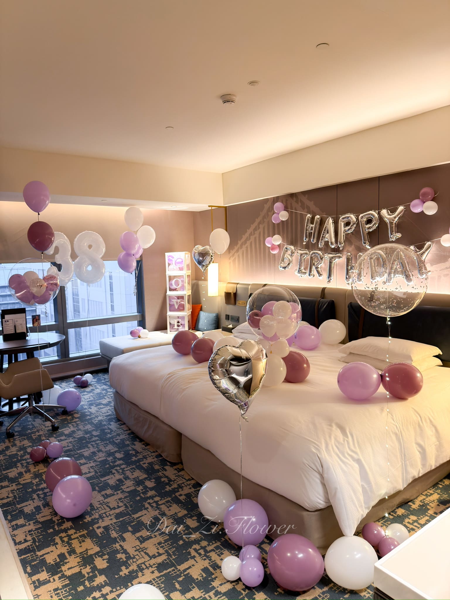 板橋新希爾頓客房生日佈置，一側有四層LOVE紫色氣球盒，床鋪與地板散落紫、白色氣球。飯店求婚佈置，板橋氣球專賣。