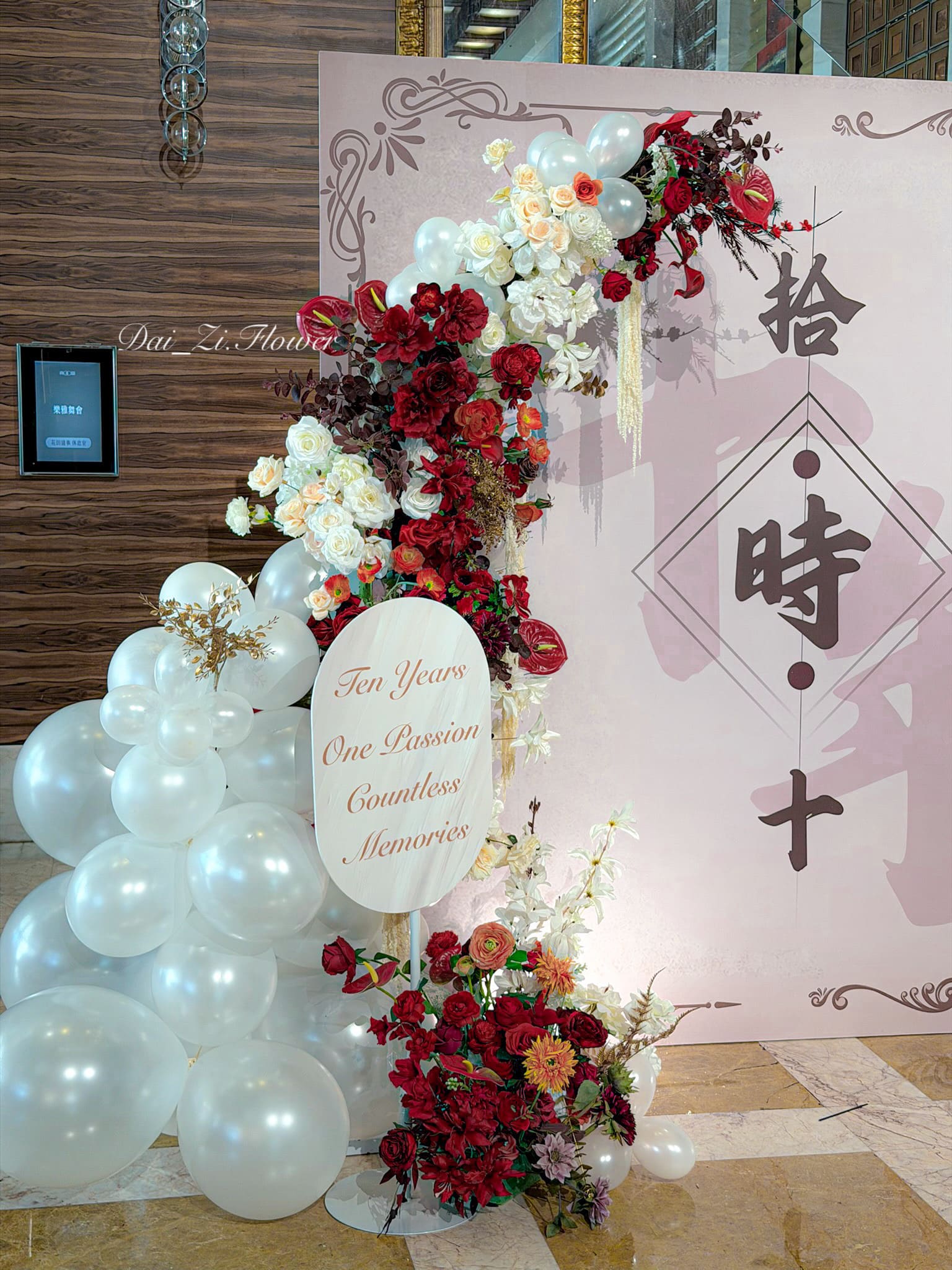 DaiZi 代紫花藝｜大直典華活動花藝氣球左側立柱特寫—酒紅深紅白色玫瑰橘色菊花混搭仿真花藝柱搭配白色氣球底座與客製橢圓形文字牌，台北舞蹈發表會花藝氣球佈置客製化